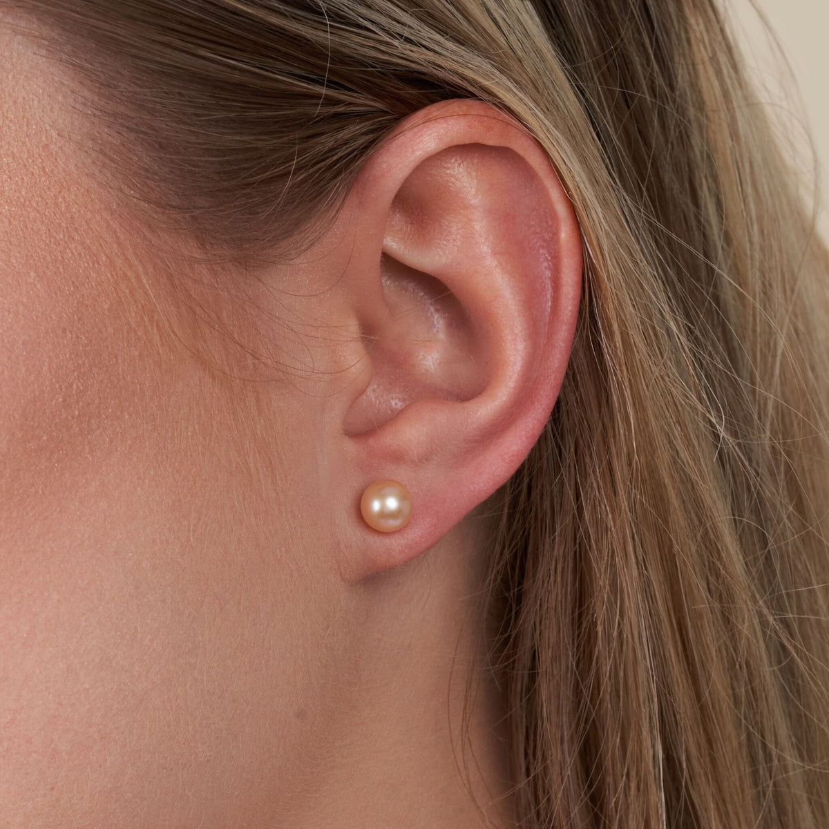 Close-up of an ear wearing a 6.5-7.0 mm AAA Pink to Peach Freshwater Pearl Stud Earrings with a soft, natural pearl luster and subtle pink to peach gradient.