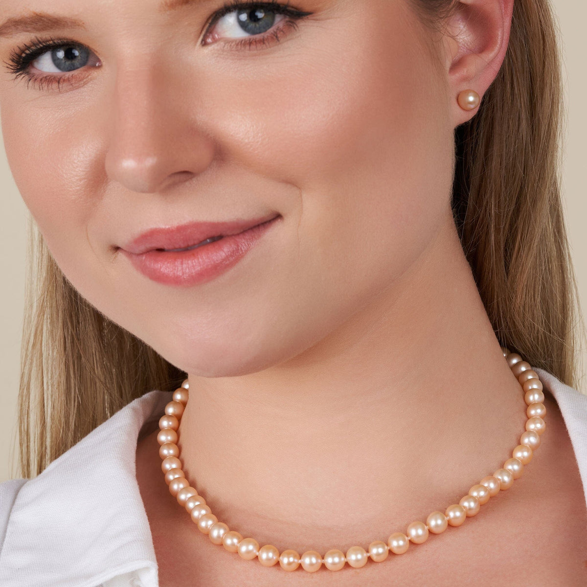 Close-up of a woman wearing a 6.5-7.0 mm AAA Pink to Peach Freshwater Pearl Necklace with matching pearl stud earrings, showcasing smooth, lustrous pearls in soft pink and peach hues.