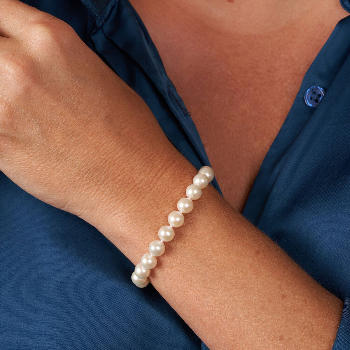 Elegant 7.5-8.0 mm AAA White Freshwater Pearl Bracelet worn on wrist with smooth, round white pearls against a navy blue blouse background, showcasing refined cultured pearls.