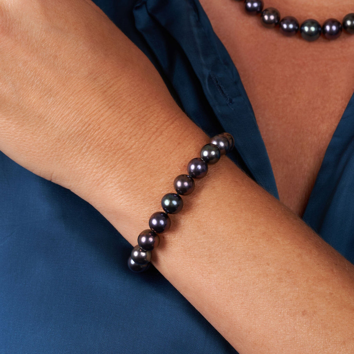 Woman wearing a 8.5-9.0 mm AAA Black Freshwater Pearl Bracelet featuring lustrous dark pearls on her wrist paired with a matching black pearl necklace against a navy blouse.