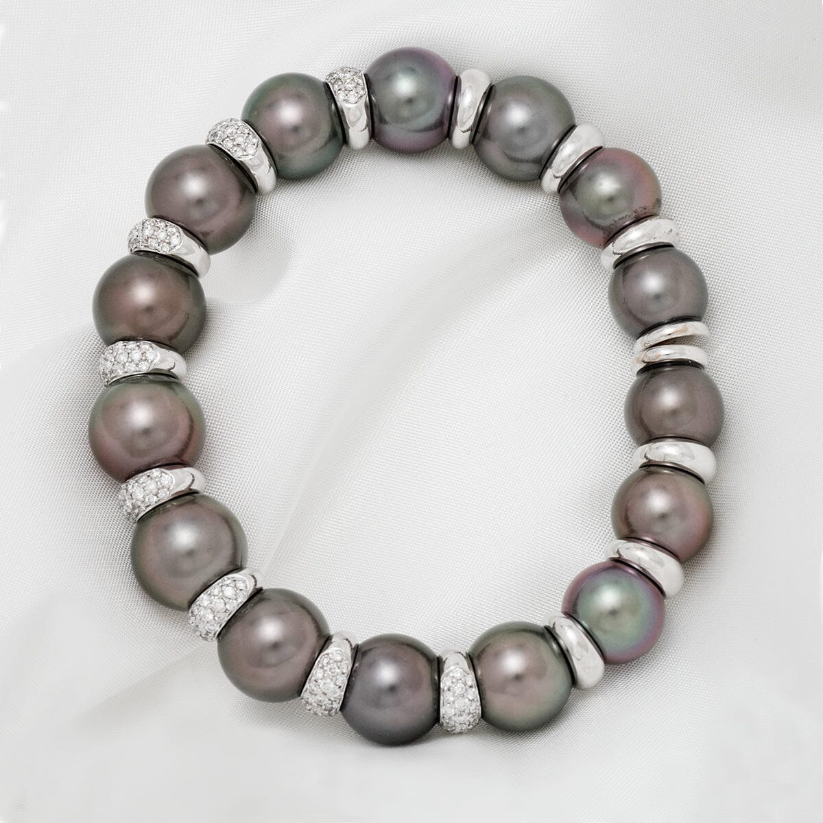 Assael Collection: 11.0-12.7 mm Tahitian Pearl and Diamond Bracelet featuring lustrous dark tahitian pearls and sparkling diamond accents on a white fabric background.