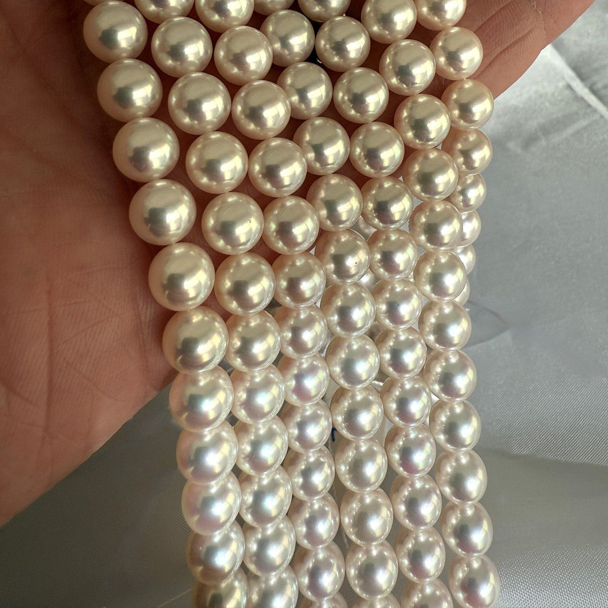 Close-up of lustrous white pearls held in hand showcasing the smooth surface and fine quality of Christina Assael Select Akoya Strands pearl necklace.