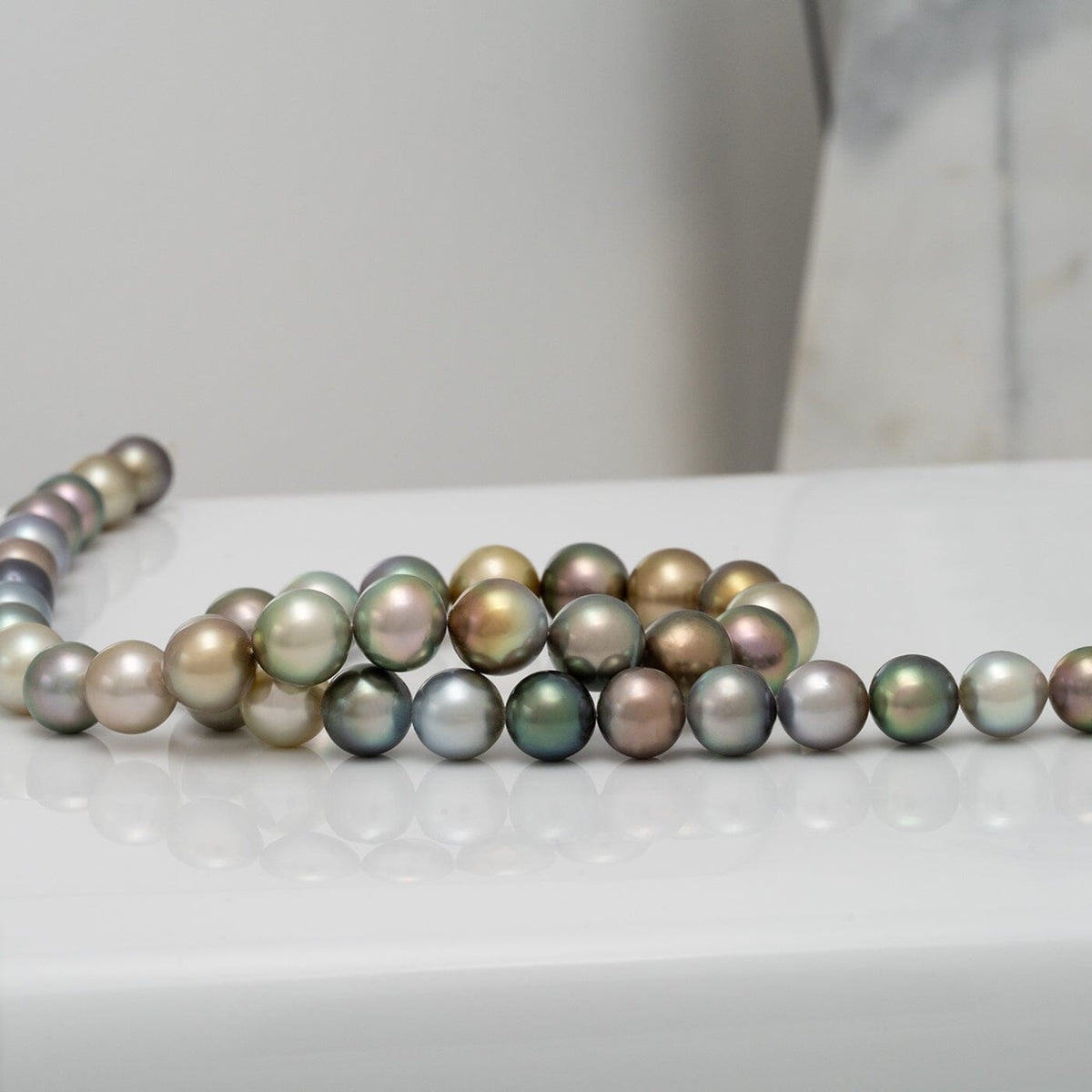 Assael Collection: 9.4–11.1 mm Fijian Pearl Necklace displayed on a white surface, featuring a luxurious strand of multicolored cultured pearls with iridescent shades of green, gold, and silver.