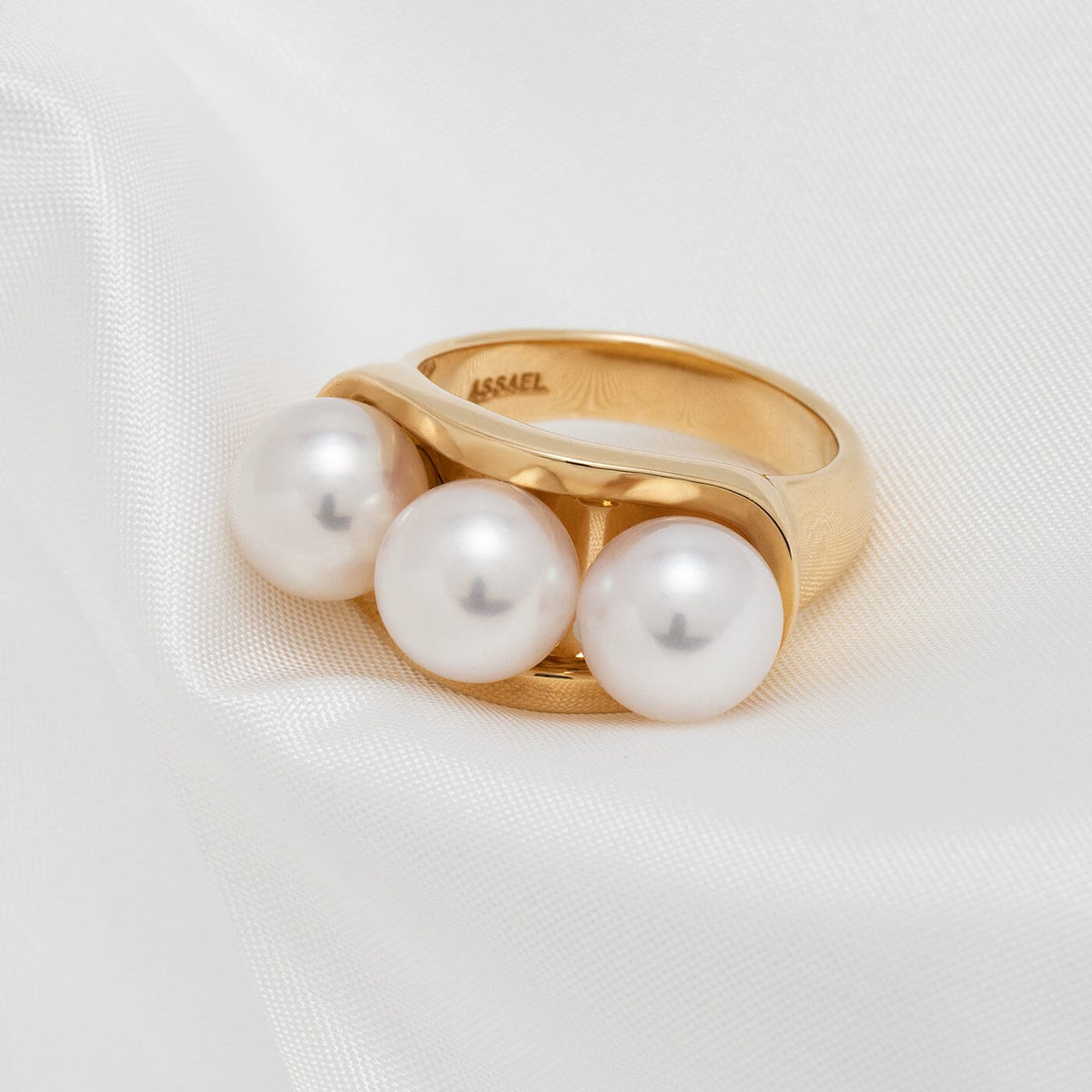 Assael Collection: 8.0–8.5 mm Akoya Three-Pearl Ring with three lustrous white akoya pearls set in a polished gold band, displayed on soft white fabric.