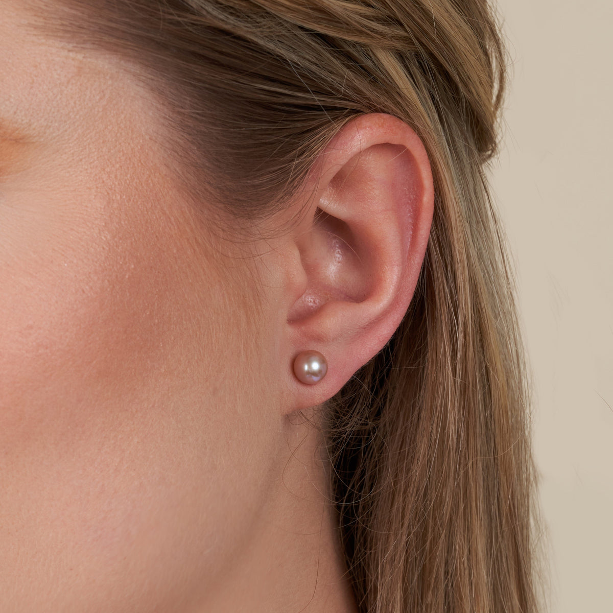 Close-up of a woman’s ear wearing 6.5-7.0 mm AAA Lavender Freshwater Pearl Stud Earrings, showcasing the smooth, lustrous lavender pearls on a neutral background.