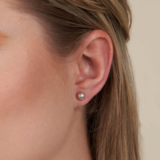 Close-up of a woman’s ear wearing 6.5-7.0 mm AAA Lavender Freshwater Pearl Stud Earrings, showcasing the smooth, lustrous lavender pearls on a neutral background.