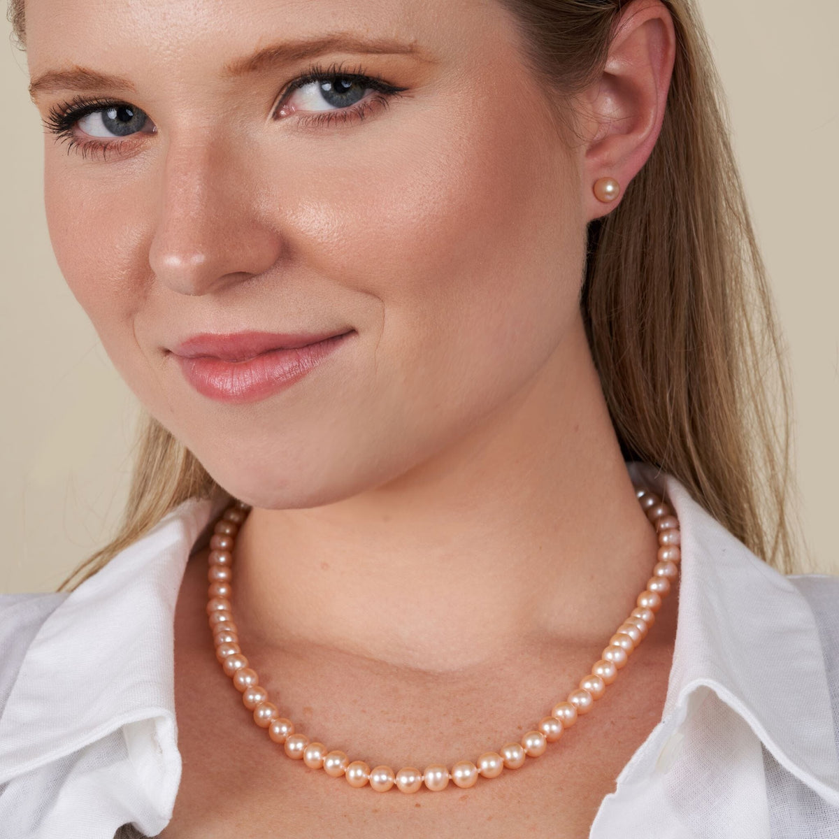 Woman wearing a 6.5-7.0 mm Pink to Peach Freshadama Freshwater Pearl Necklace with matching pearl stud earrings, styled with a white blouse.