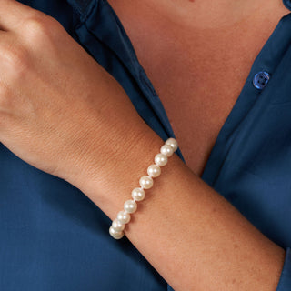 Elegant 7.5-8.0 mm AAA White Freshwater Pearl Bracelet worn on wrist with smooth, round white pearls against a navy blue blouse background, showcasing refined cultured pearls.