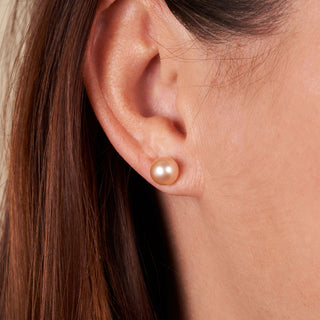 Close-up of a delicate 7.5-8.0 mm AAA Pink to Peach Freshwater Pearl Stud Earrings worn on an ear, showcasing their soft luster and elegant, natural color.
