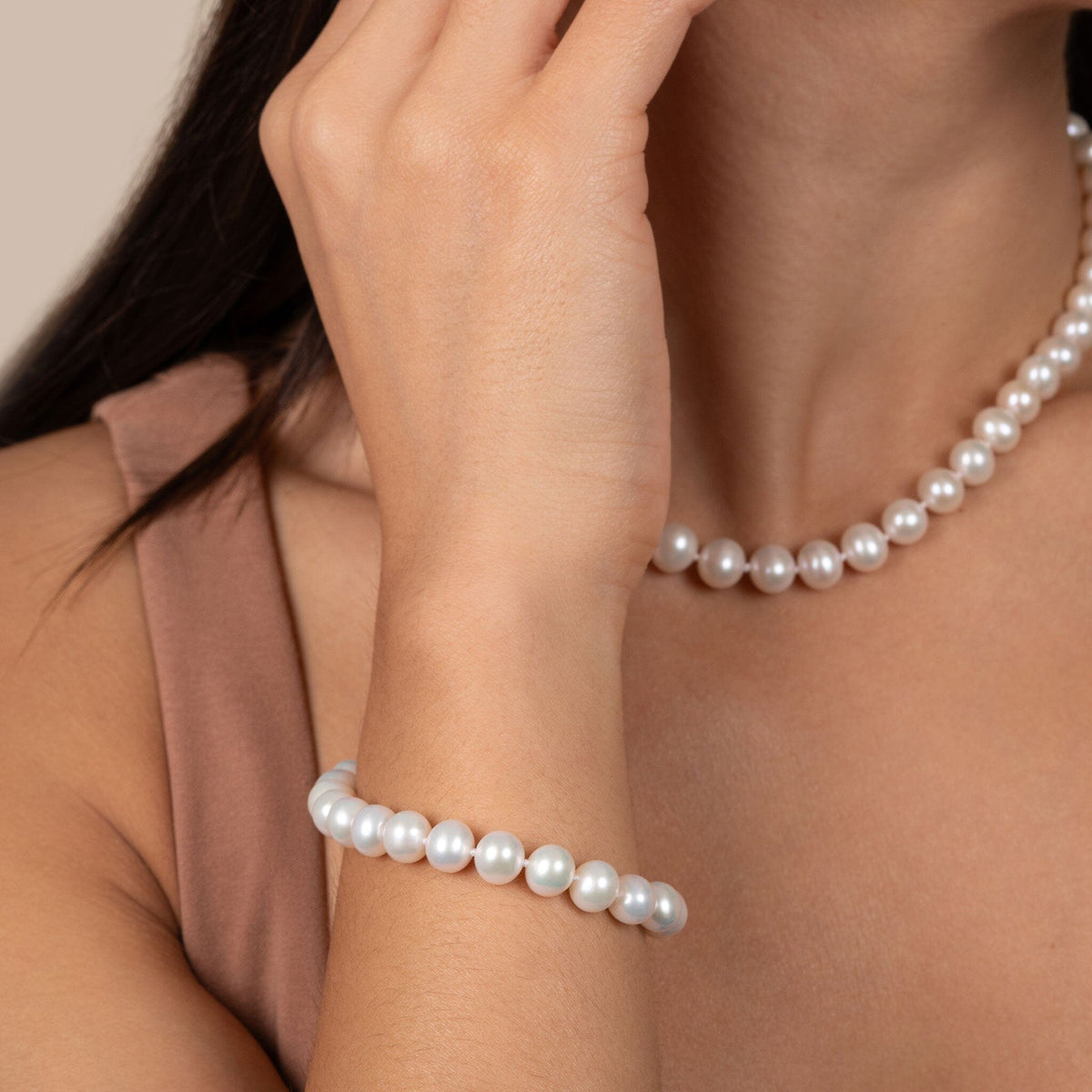 Woman wearing a 7.5-8.0 mm White Freshwater AA+ Pearl Bracelet with matching white freshwater pearl necklace, showcasing elegant cultured pearls on her wrist.