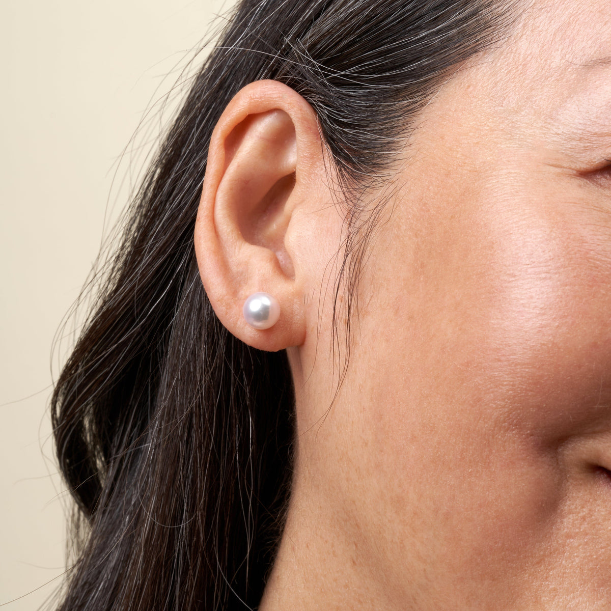 Close-up of a woman wearing 8.0-8.5 mm White Akoya AAA Pearl Stud Earrings, showing the elegant white cultured pearls against her skin and dark hair.