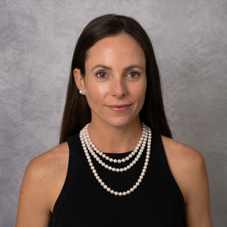 Woman wearing a 3-Piece Set of 8.0-8.5 mm AAA White Akoya Pearls necklace and matching pearl earrings, showcasing lustrous white cultured pearls against a black top.