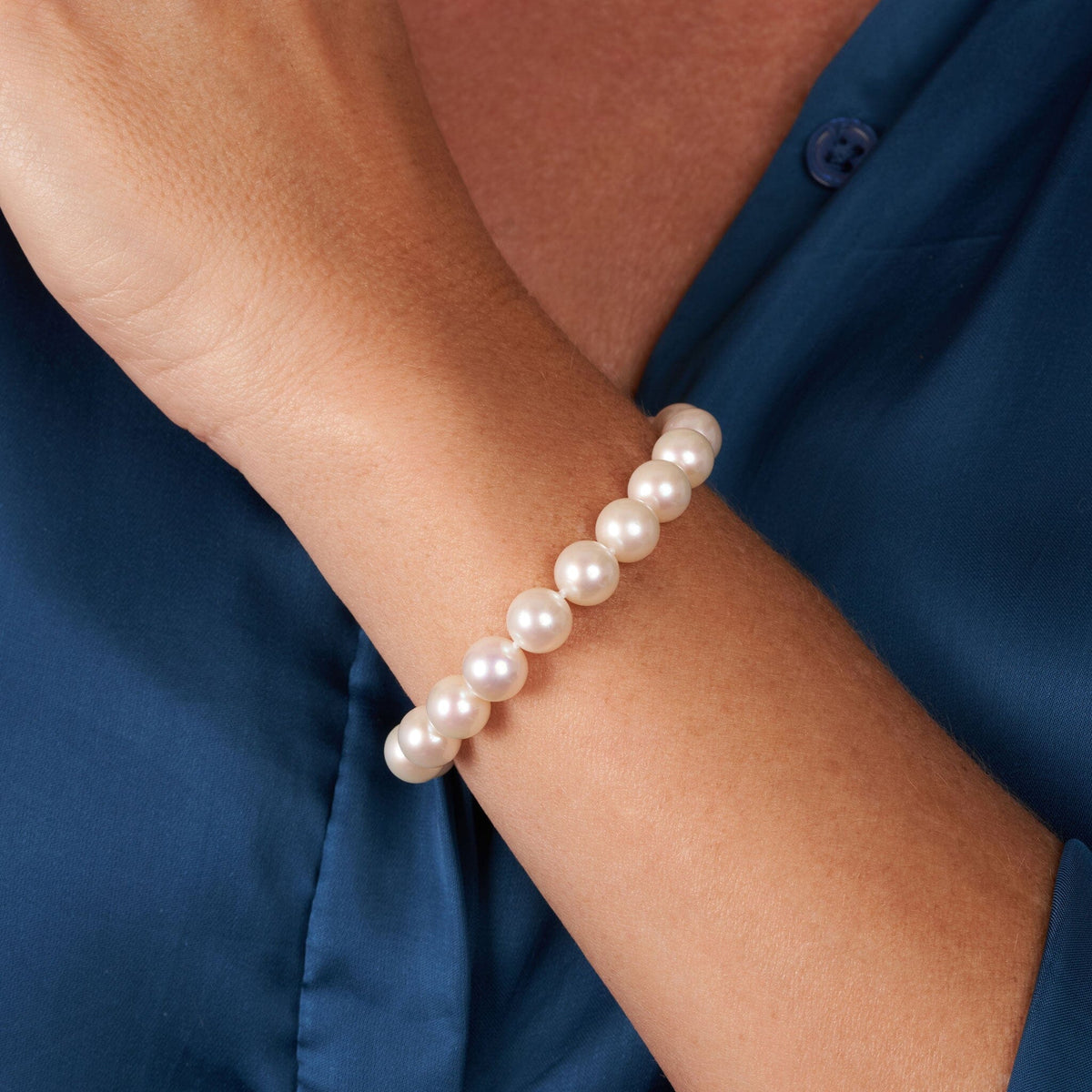 Elegant 8.5-9.0 mm AAA White Freshwater Pearl Bracelet worn on wrist, showcasing lustrous round white pearls with smooth surface and classic design against a navy blue shirt background.