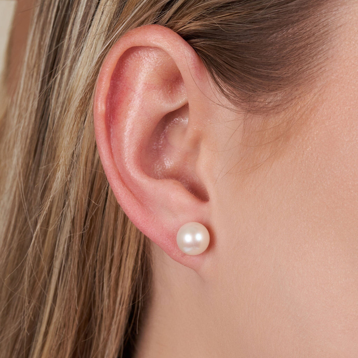 Close-up of a woman’s ear wearing 8.5-9.0 mm AAA White Freshwater Pearl Stud Earrings, showcasing the lustrous round white pearl on a simple stud setting.