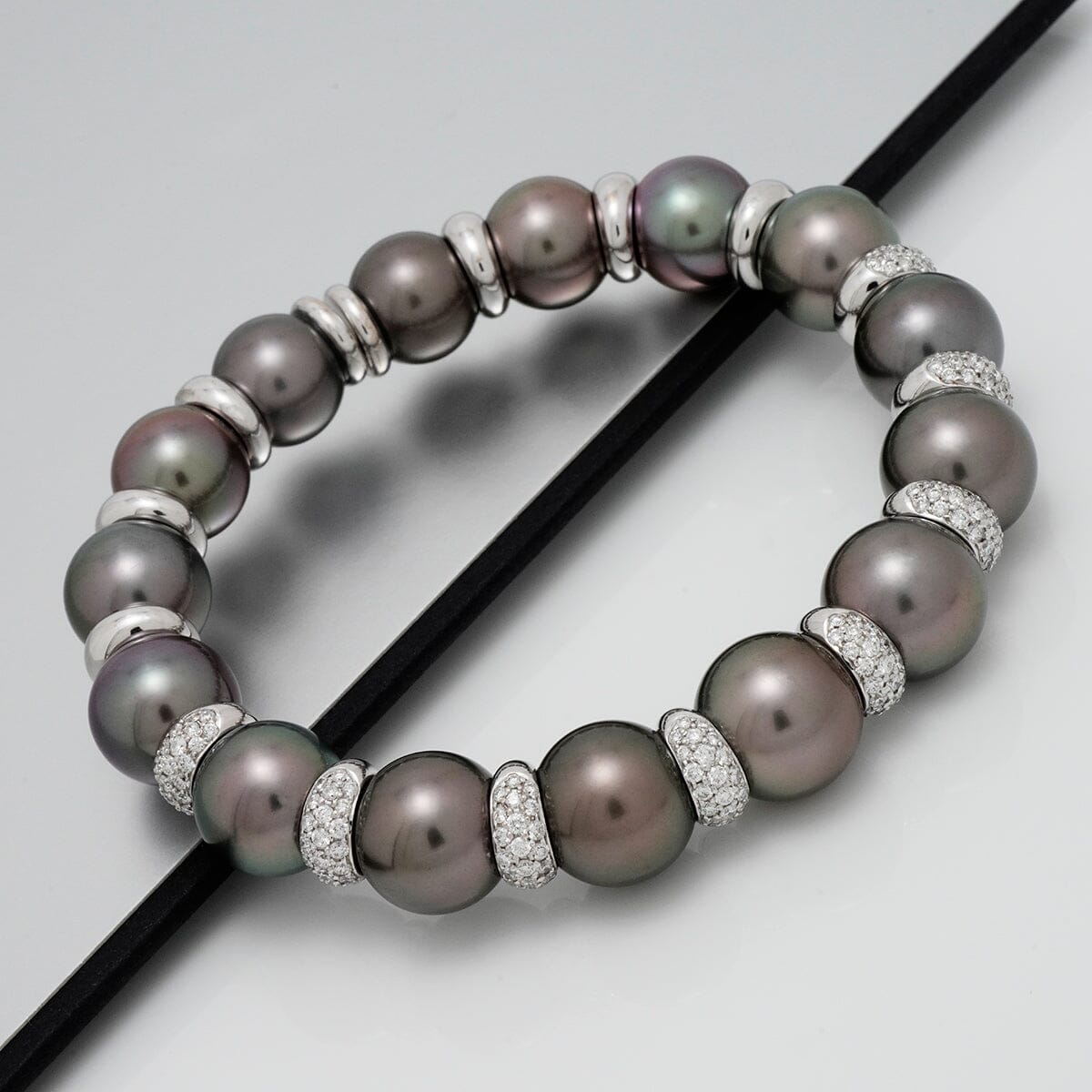 Assael Collection: 11.0-12.7 mm Tahitian Pearl and Diamond Bracelet featuring lustrous dark Tahitian pearls separated by sparkling diamond-encrusted spacers on a sleek surface.