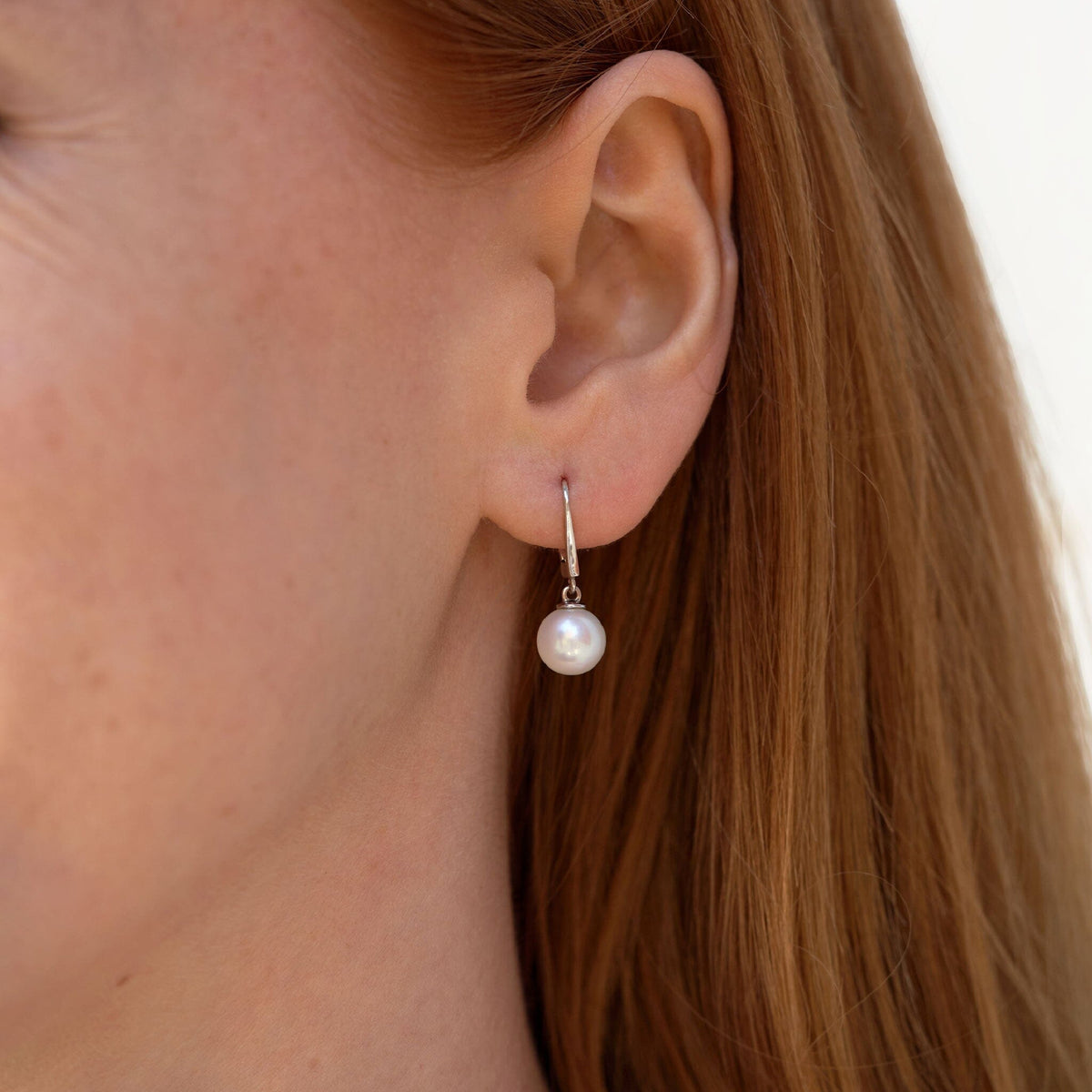 Close-up of an ear wearing Classic Collection White Freshadama Freshwater 8.5-9.0 mm Pearl Dangle Earrings with a single elegant white pearl hanging from a delicate 14K white gold hook.