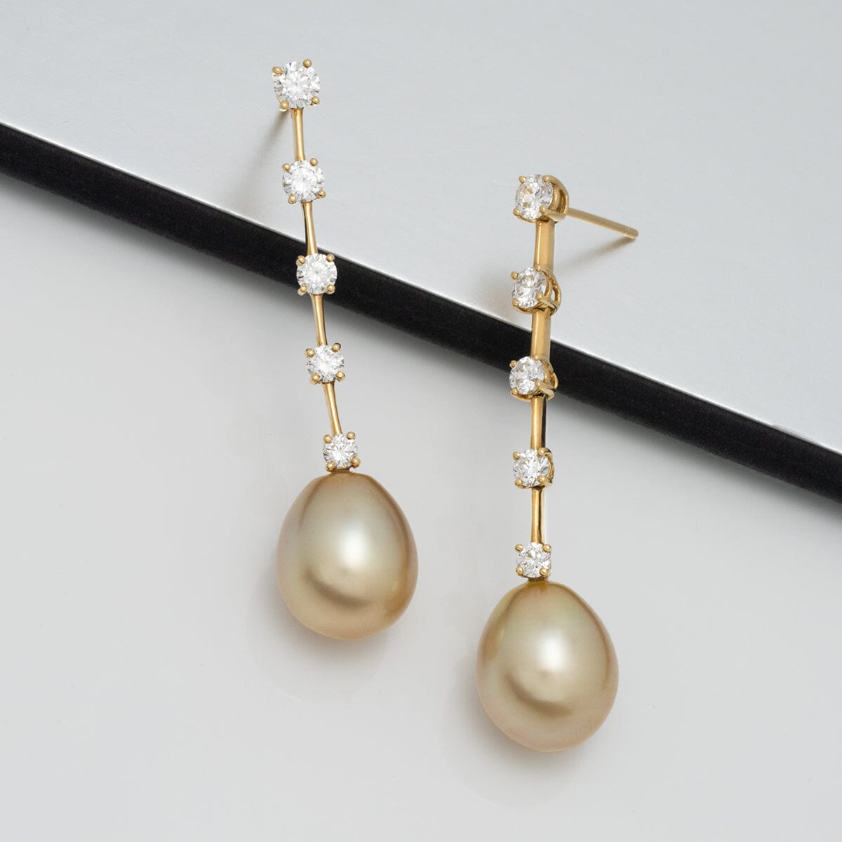 Assael Collection: 11.2 x 13.6 mm Golden South Sea Pearl and Diamond Earrings featuring elegant golden pearls hanging from a slender gold bar adorned with sparkling diamonds.