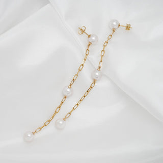 Assael Collection: 7.5-8.0 mm Akoya Pearl Dangle Earrings featuring elegant white pearls suspended on delicate gold chain links against a soft white fabric background.