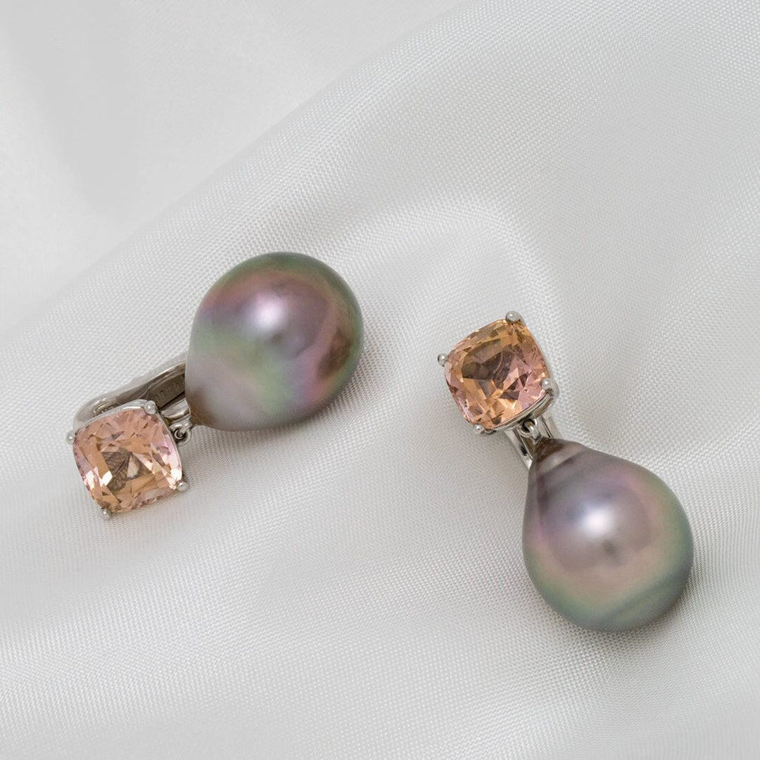 Pair of Assael Collection: 16.3x13.0 mm Tahitian Pearl and Tourmaline Earrings featuring lustrous black pearls and soft peach tourmaline gemstones on a white fabric background.