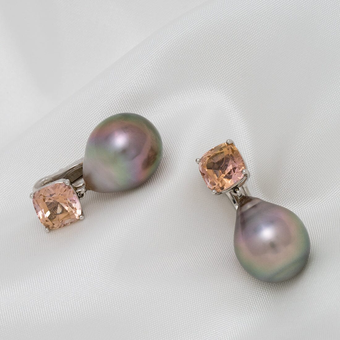 Pair of Assael Collection: 16.3x13.0 mm Tahitian Pearl and Tourmaline Earrings featuring lustrous black pearls and soft peach tourmaline gemstones on a white fabric background.