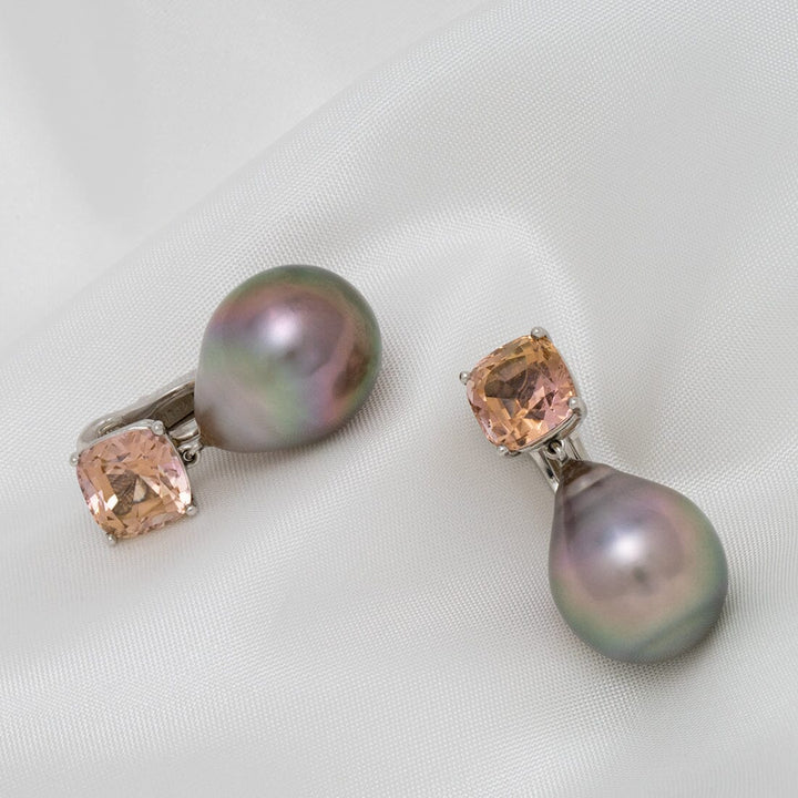 Pair of Assael Collection: 16.3x13.0 mm Tahitian Pearl and Tourmaline Earrings featuring lustrous black pearls and soft peach tourmaline gemstones on a white fabric background.