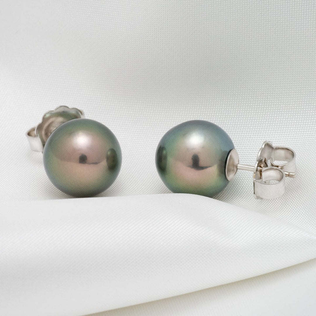 Assael Collection: 12.0–13.0 mm Tahitian Pearl Stud Earrings featuring lustrous round pearls with subtle green and lavender overtones set on silver posts against a white fabric background.