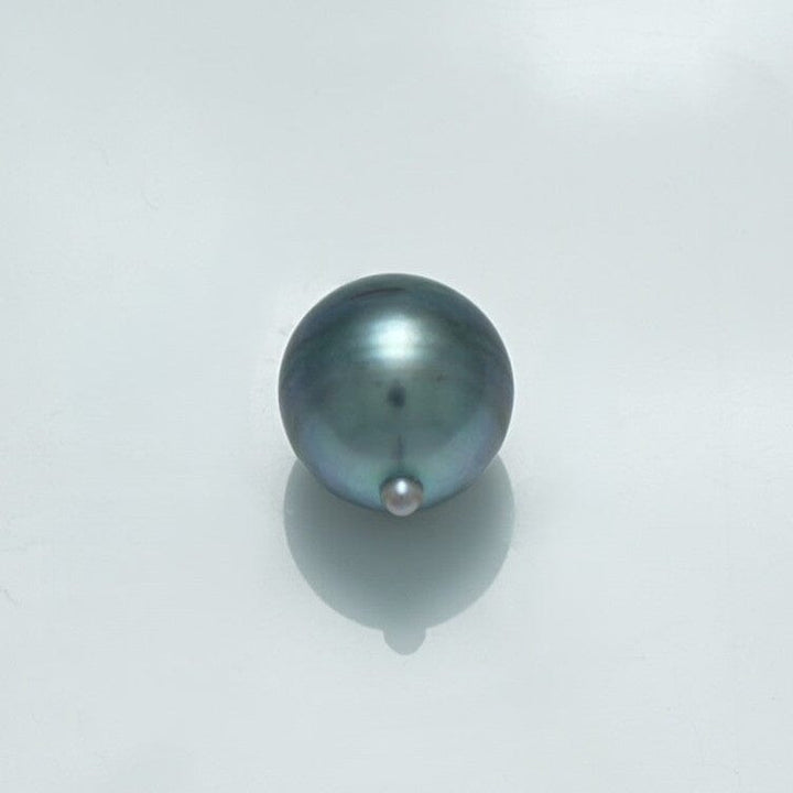 11.5 x 10.0 mm Fijian Drop Pearl with a smooth, lustrous surface showcasing natural hues of dark gray and subtle iridescent tones on a light background.