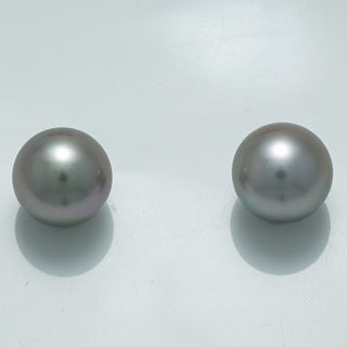 10.1 x 10.0 mm and 10.0 x 10.0 mm Fijian Pearl Pair showcasing two lustrous, round, dark gray cultured pearls with subtle green and purple overtones on a reflective white surface.