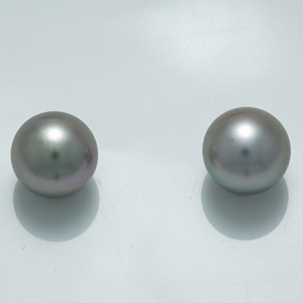 10.1 x 10.0 mm and 10.0 x 10.0 mm Fijian Pearl Pair showcasing two lustrous, round, dark gray cultured pearls with subtle green and purple overtones on a reflective white surface.