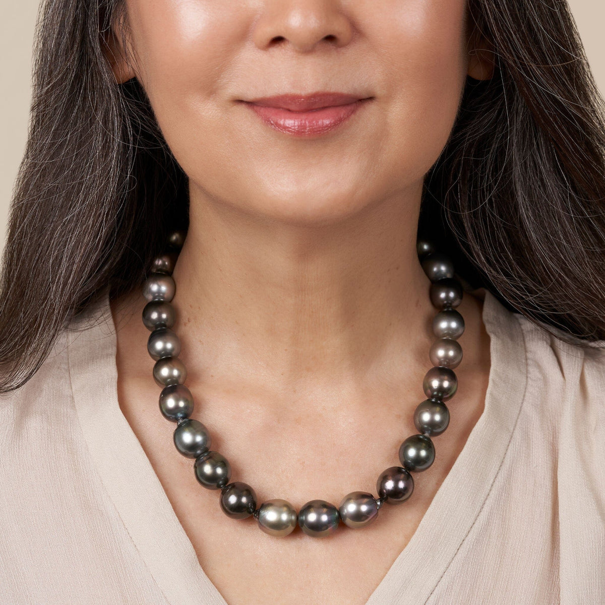 Woman wearing a 14.0-16.0 mm AA+/AAA Tahitian Drop Pearl Necklace featuring lustrous black and dark gray pearls against a neutral beige top.