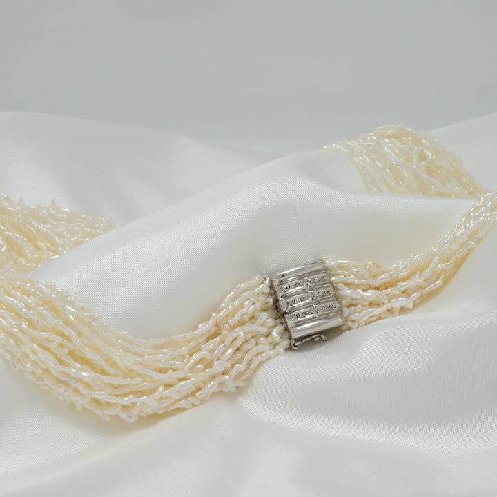 1.0-3.0 mm 20 Strand Akoya Keshi Pearl Torsade Diamond Clasp Necklace with creamy white cultured pearls and an elegant diamond-accented clasp resting on soft white fabric.
