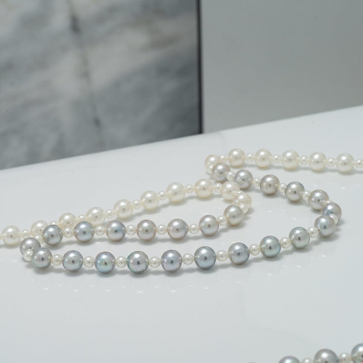 Close-up of a luxurious 2.0-5.5 mm Intense Blue Ombre Akoya Semi-Round Pearl Strand featuring lustrous pearls in shades of white, silver, and blue on a polished surface.