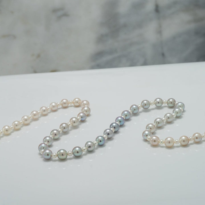 Close-up of a 2.0-5.5 mm Intense Blue Ombre Akoya Semi-Round Pearl Strand showcasing graduated pearls with iridescent blue and white hues on a smooth surface.