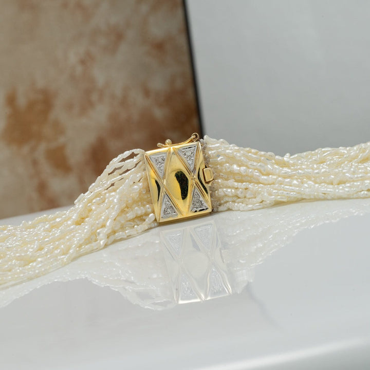 Close-up of the 1.0-3.0 mm 20 Strand Akoya Keshi Pearl Torsade Diamond Clasp Necklace featuring delicate white pearls and a gold and diamond geometric clasp resting on a reflective surface.