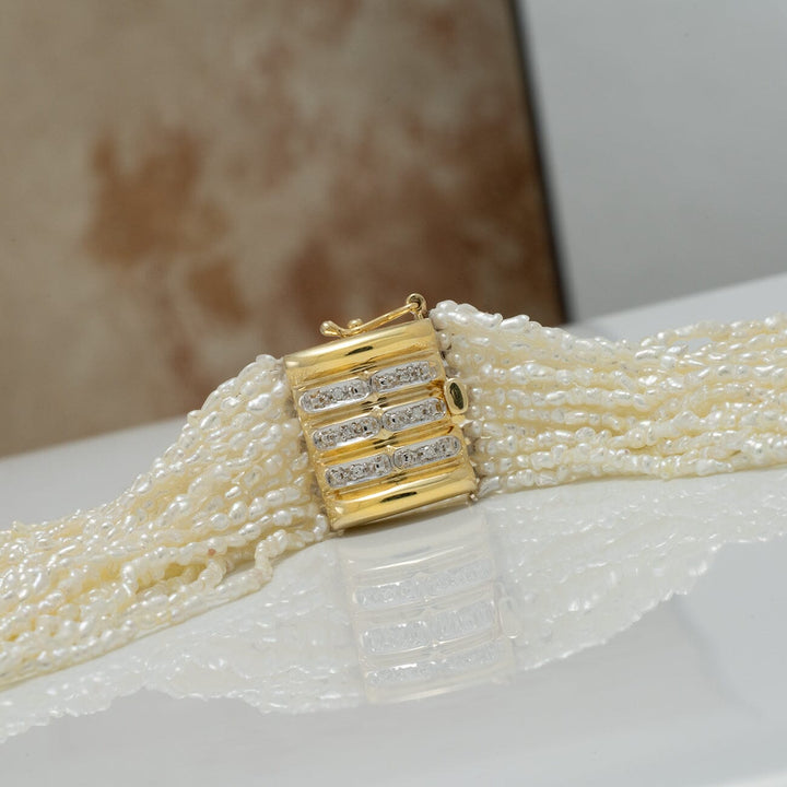 Close-up of the 1.0-3.0 mm 20 Strand Akoya Keshi Pearl Torsade Diamond Clasp Necklace featuring multiple strands of lustrous white pearls with a gold and diamond clasp on a reflective surface.