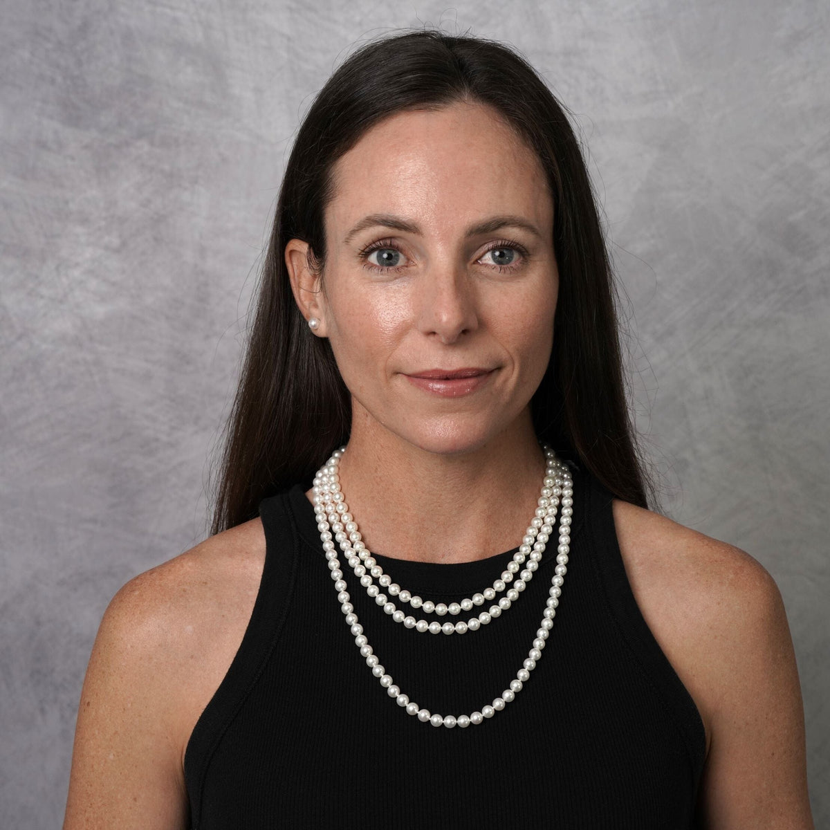 Woman wearing a 3-Piece Set of 6.5-7.0 mm AAA White Akoya Pearls necklace and matching pearl stud earrings, styled with a black sleeveless top against a neutral background.