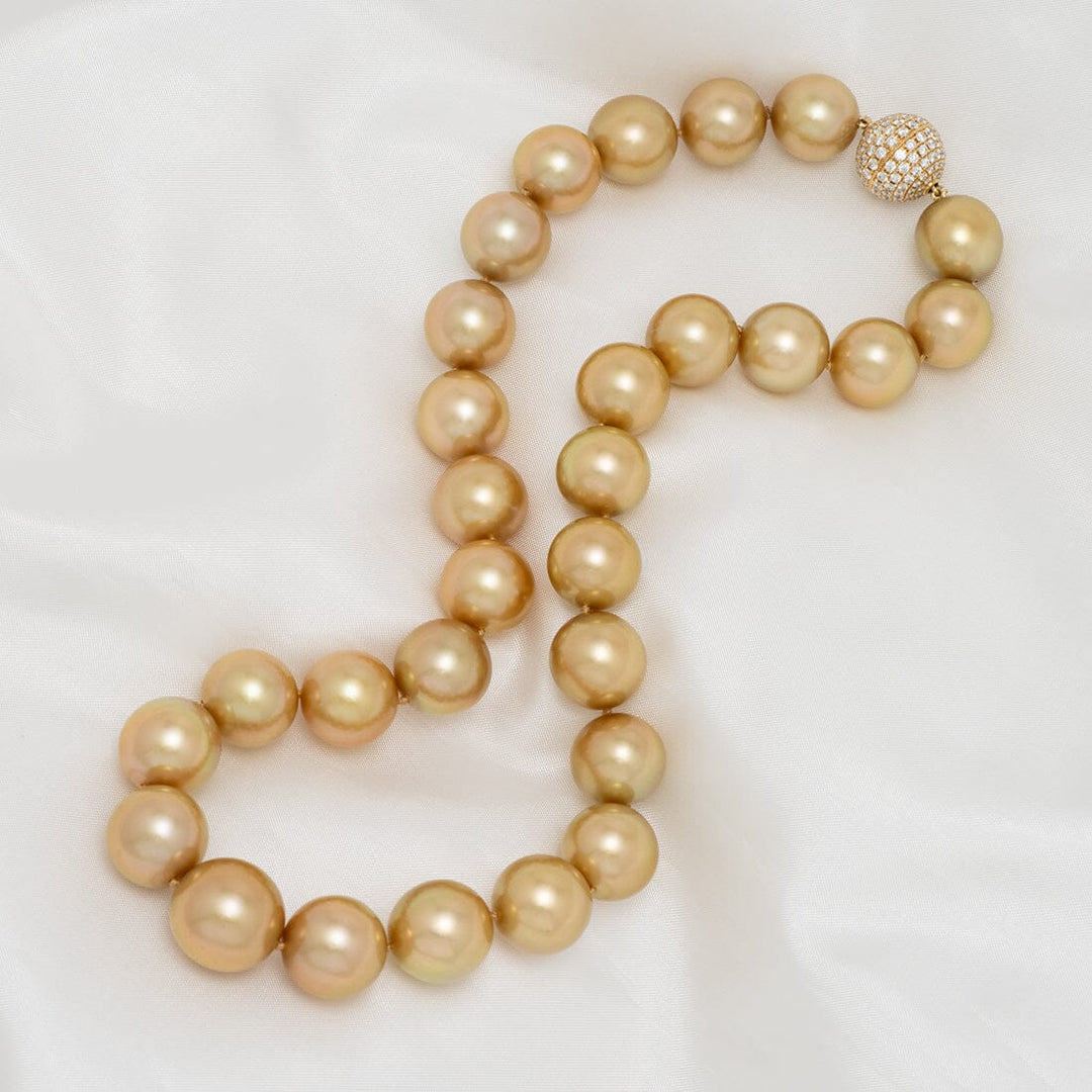 Assael Collection: 13.0–15.1 mm Round Golden South Sea Pearl Necklace elegantly displayed on a soft white fabric, featuring lustrous golden pearls and a decorative clasp.