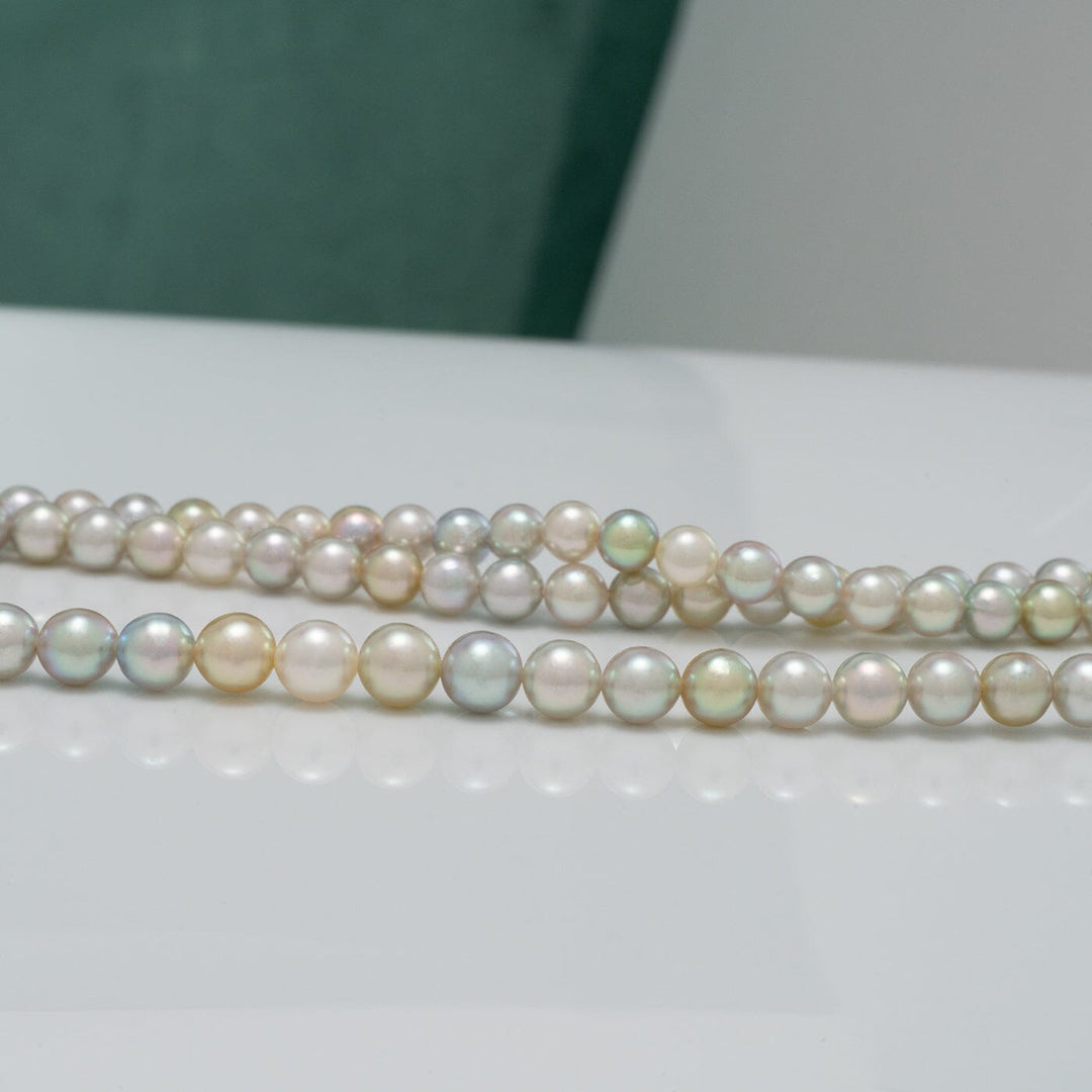 TF-26: 4-5 mm Natural Multicolor Akoya Pearl Round Strands featuring lustrous round pearls in soft shades of white, cream, pink, and subtle green hues on a reflective surface.