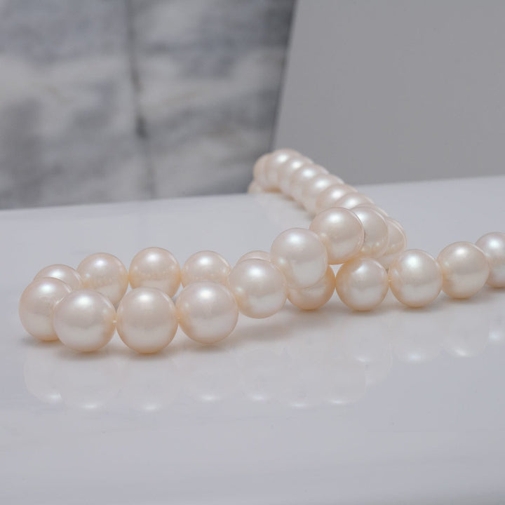Close-up view of lustrous white pearls arranged in a strand showcasing the 10.5-11.5 mm AA+ White Freshwater Pearl Necklace with a smooth, reflective surface.