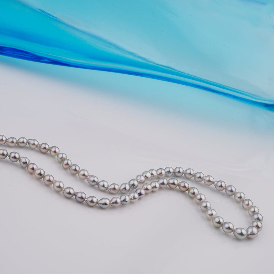 B-12: 3-4.5 mm Silver-blue Drop Akoya Strands, 16-inch Unfinished Strand displayed against a soft blue background, showcasing lustrous cultured pearls.