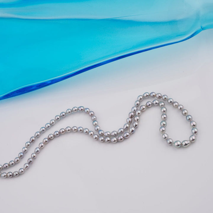 B-13: 3-4.5 mm Blue-silver Drop Akoya Strands, 16-inch Unfinished Strand displayed on a light surface with a translucent blue accent, showcasing lustrous round cultured pearls.