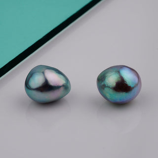 B-9: 9.0-9.5 mm Baroque Blue Akoya Pearl Pairs showing two irregularly shaped pearls with iridescent blue and green hues on a reflective surface.