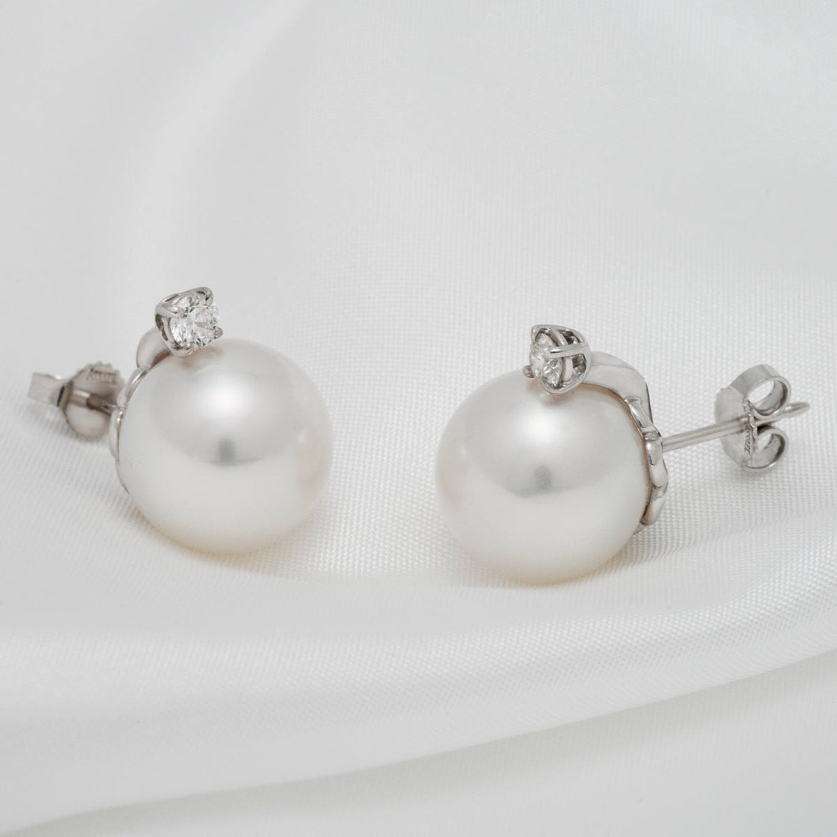 Assael Collection: 13.0 mm White South Sea Pearl and Diamond Earrings featuring lustrous white pearls set with sparkling diamonds on a 18K white gold backing, displayed on a white fabric background.