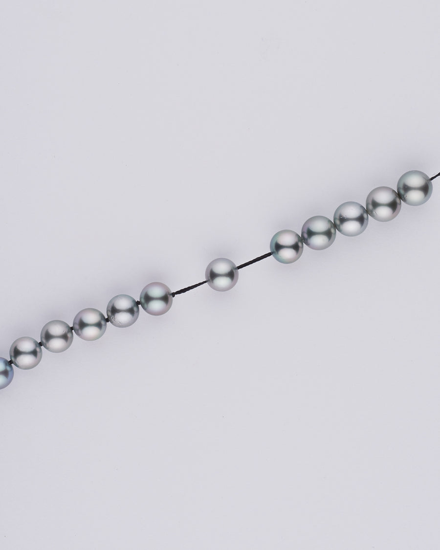 A pearl strand being hand-knotted, one knot between each pearl