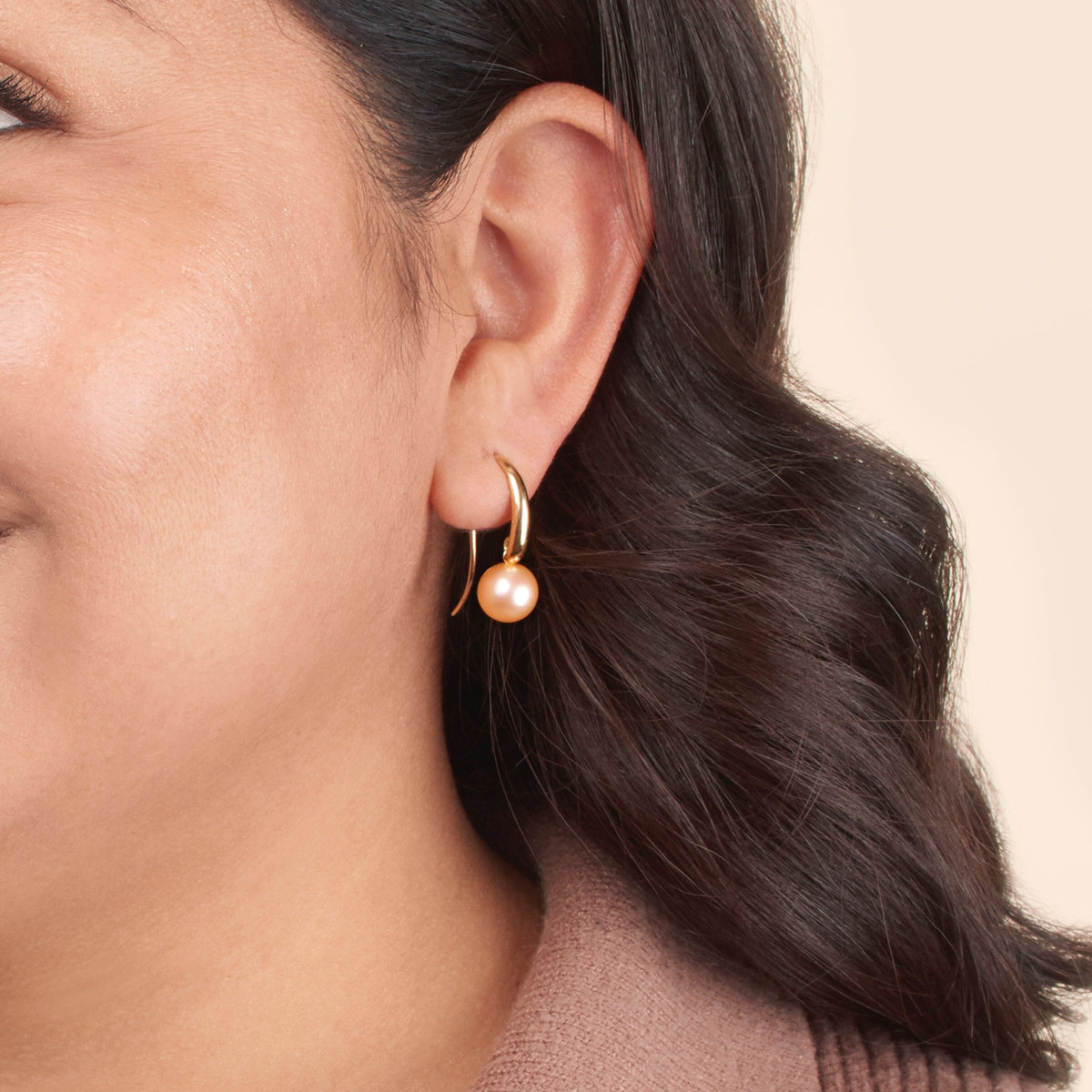 Close-up of a woman wearing Cascade Collection 8.5-9.0 mm Pink Freshadama Pearl Earrings with a gold setting, showcasing the elegant pink freshwater pearls against a neutral background.