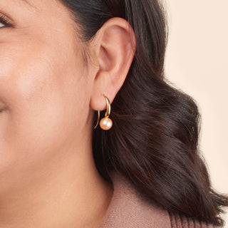 Close-up of a woman wearing Cascade Collection 8.5-9.0 mm Pink Freshadama Pearl Earrings with a gold setting, showcasing the elegant pink freshwater pearls against a neutral background.