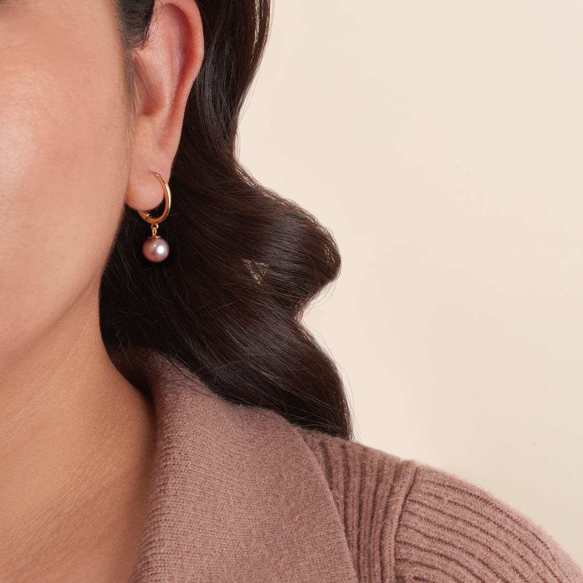 Close-up of a woman wearing Solid Eternal Collection 7.5-8.0 mm White Freshadama Pearl Earrings with gold hoops and a single white freshwater pearl drop against a neutral background.